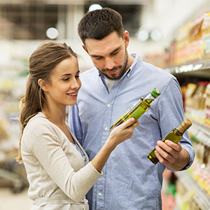 A young couple in a grocery store setting viewing nutrition facts for olive oil products.